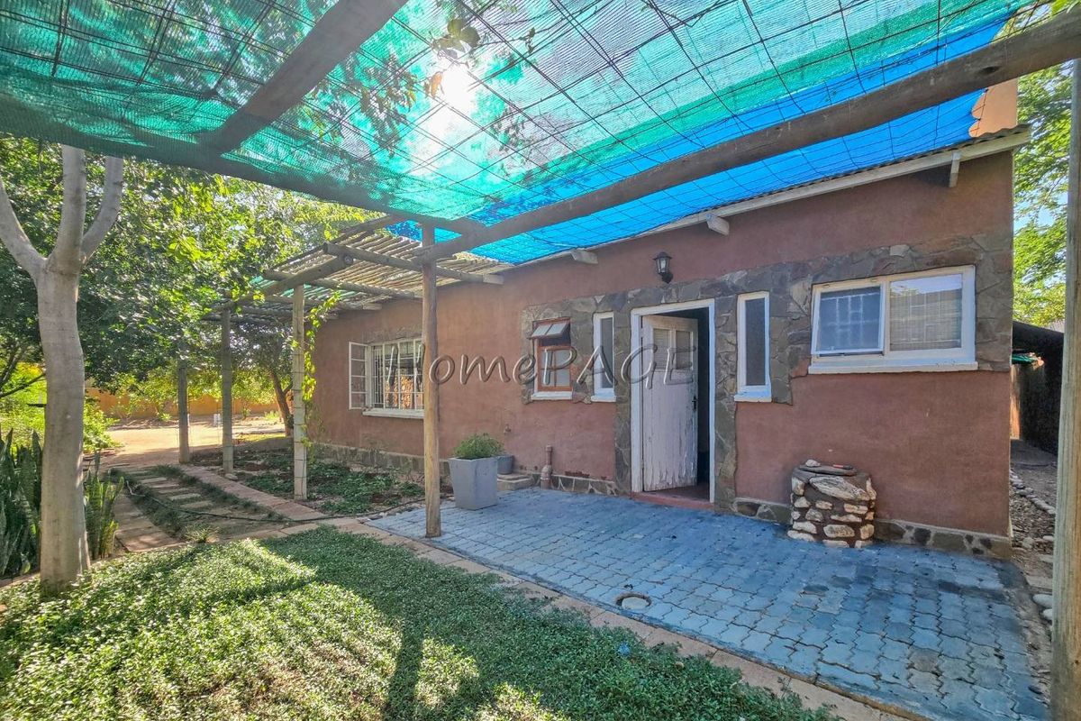 A rear exterior view featuring a paved patio area, stone-accented facade, and overhead shade netting structure.