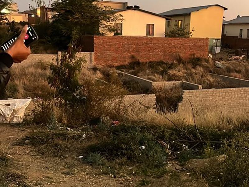Vacant residential land featuring a concrete foundation and brick boundary wall, currently overgrown with vegetation and requiring site clearance.