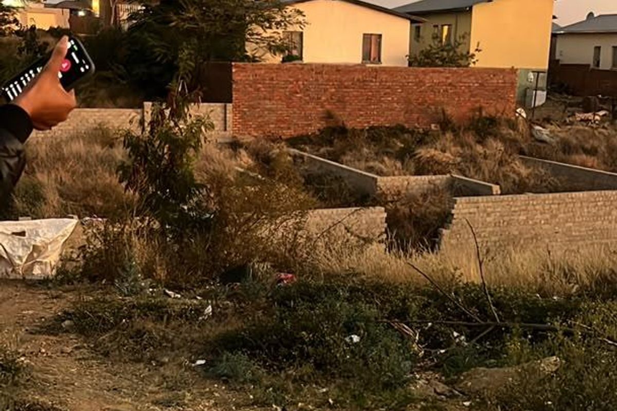 Vacant residential land featuring a concrete foundation and brick boundary wall, currently overgrown with vegetation and requiring site clearance.