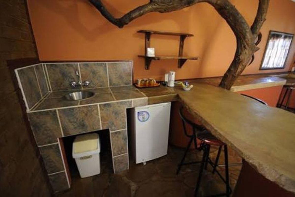 A rustic kitchen area featuring a tiled countertop with an integrated sink, floating wooden shelving, and a unique concrete breakfast bar.