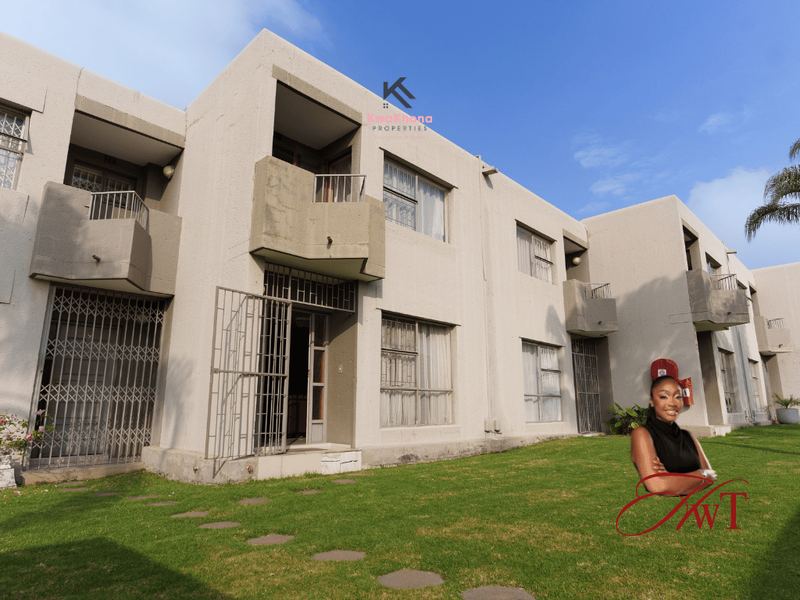 Rear view of a multi-story townhouse complex featuring concrete facade, private balconies, security gates, and a shared lawn area.