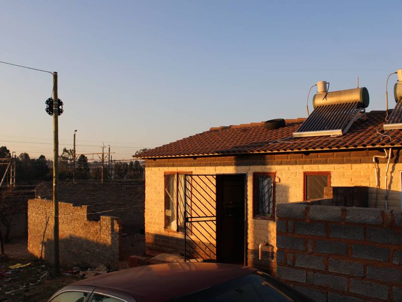 Rear view of a brick house featuring a solar water heating system on a tiled roof and a security gate at the entrance.