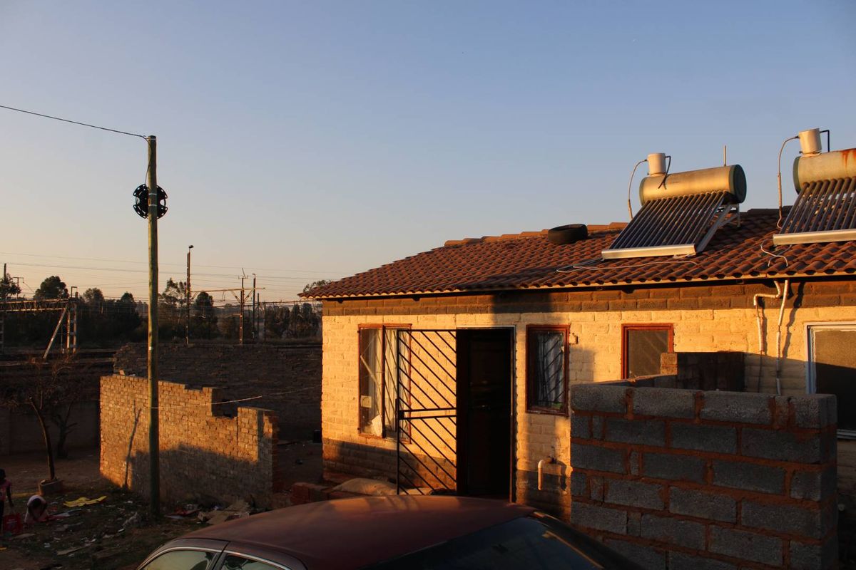 Rear view of a brick house featuring a solar water heating system on a tiled roof and a security gate at the entrance.