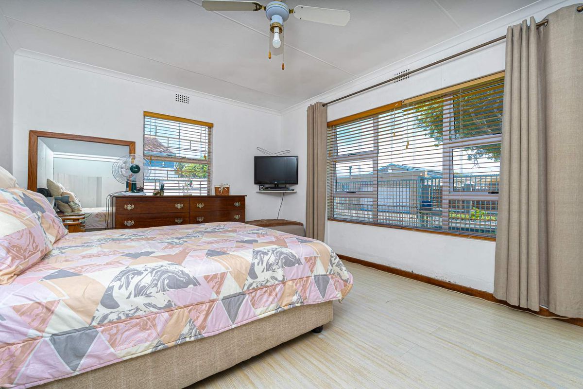 A bedroom featuring large windows with blinds, a ceiling fan, and neutral wall finishes.