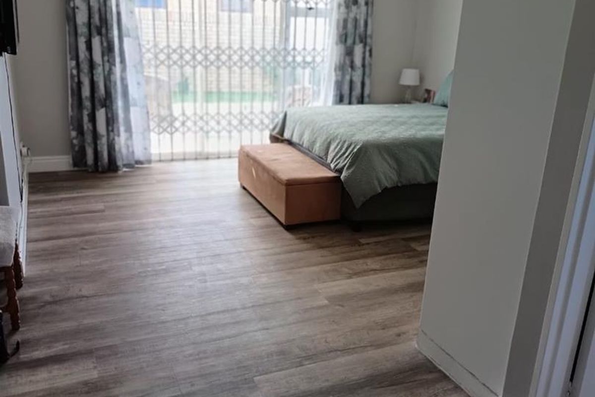 Spacious bedroom featuring modern laminate flooring, neutral wall tones, and a large sliding glass door with security gate providing access to the exterior.