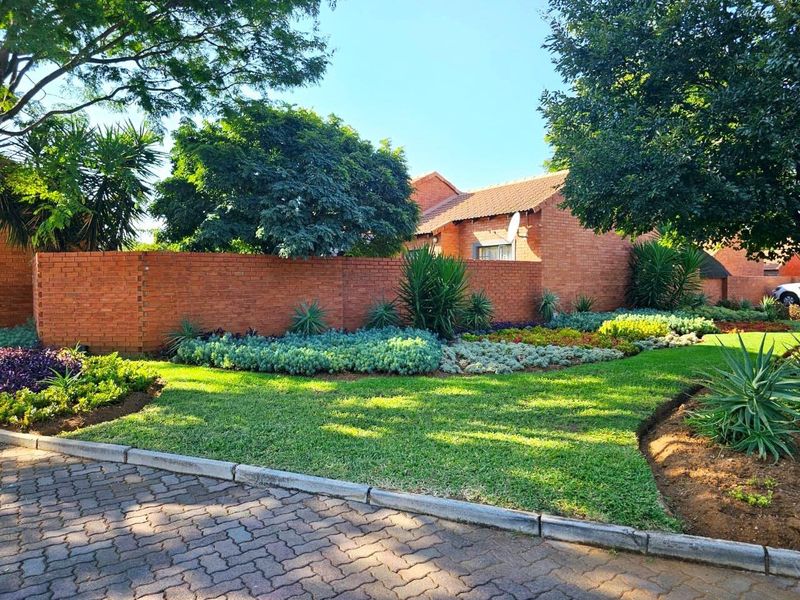 A well-maintained front exterior view of the townhouse featuring a neat brick boundary wall, established garden, and paved driveway access.