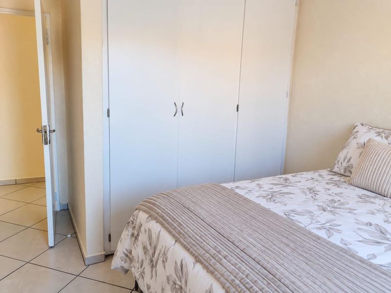 A bedroom featuring neutral wall tones, tiled flooring, and a built-in wardrobe with white doors.
