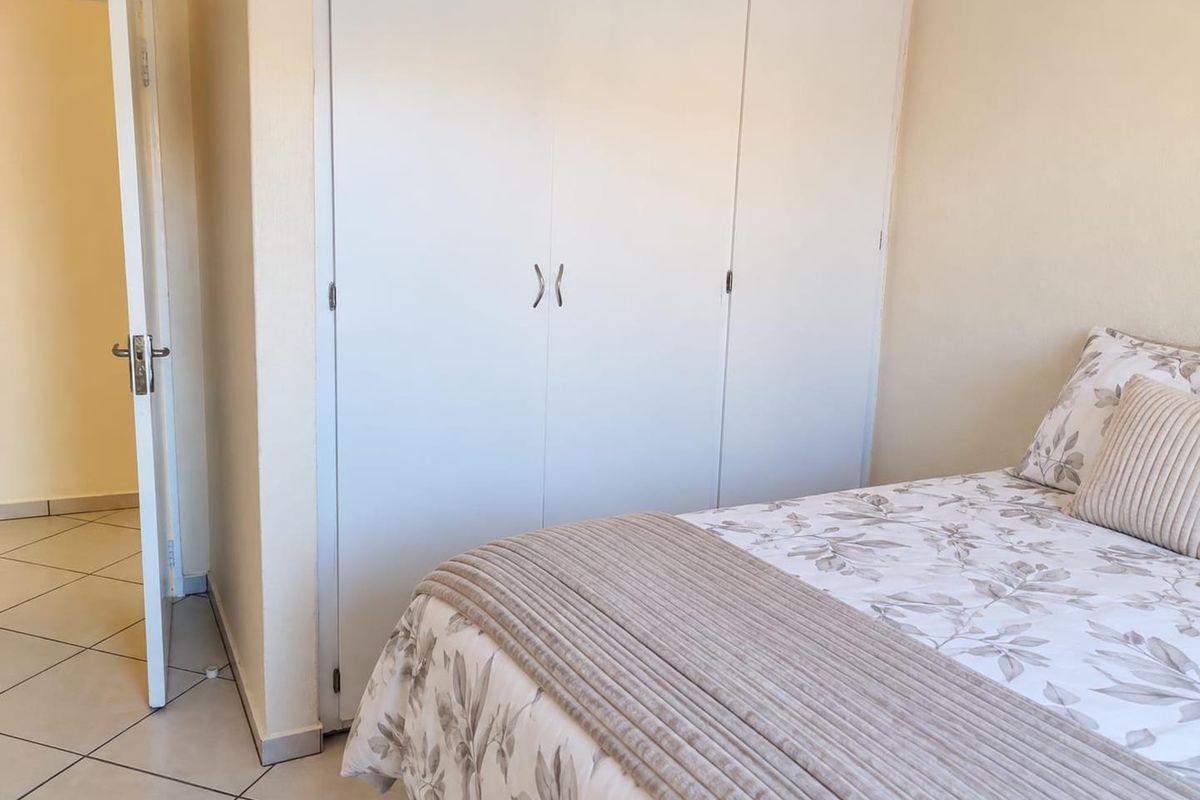 A bedroom featuring neutral wall tones, tiled flooring, and a built-in wardrobe with white doors.