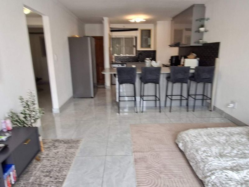 Open-plan living area featuring a modern kitchen with a breakfast bar and tiled flooring throughout, creating a functional and connected living space.