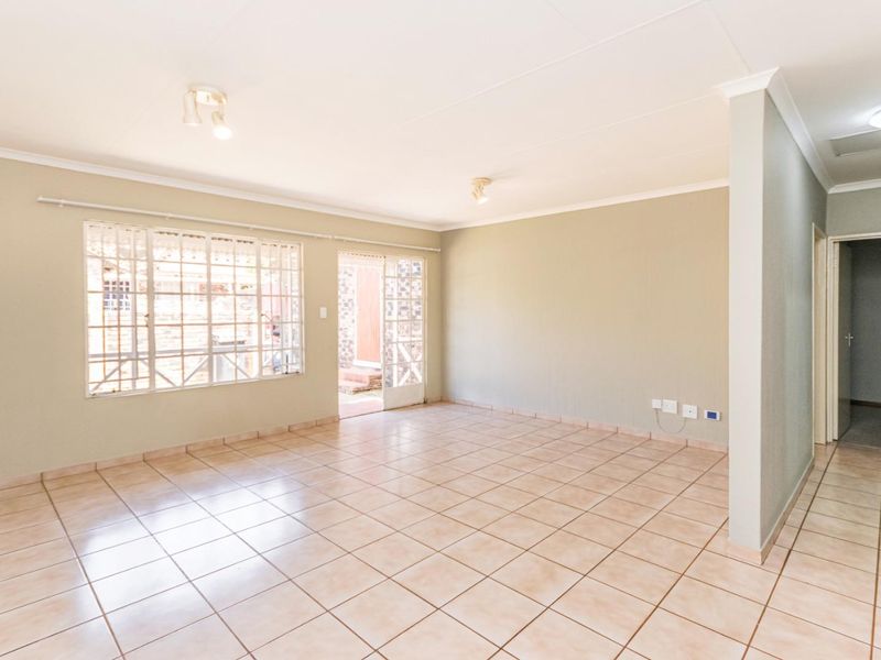 A spacious, empty living area featuring neutral tiled flooring, security bars on windows, and direct access to an outdoor space.