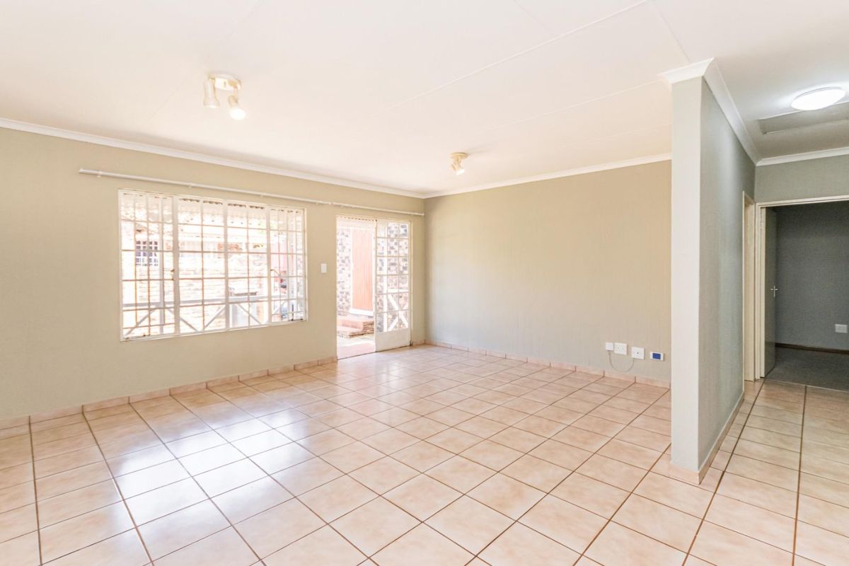 A spacious, empty living area featuring neutral tiled flooring, security bars on windows, and direct access to an outdoor space.