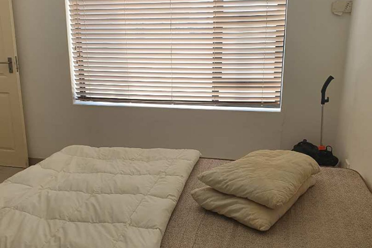 A bedroom featuring a window with fitted venetian blinds and neutral wall finishes.