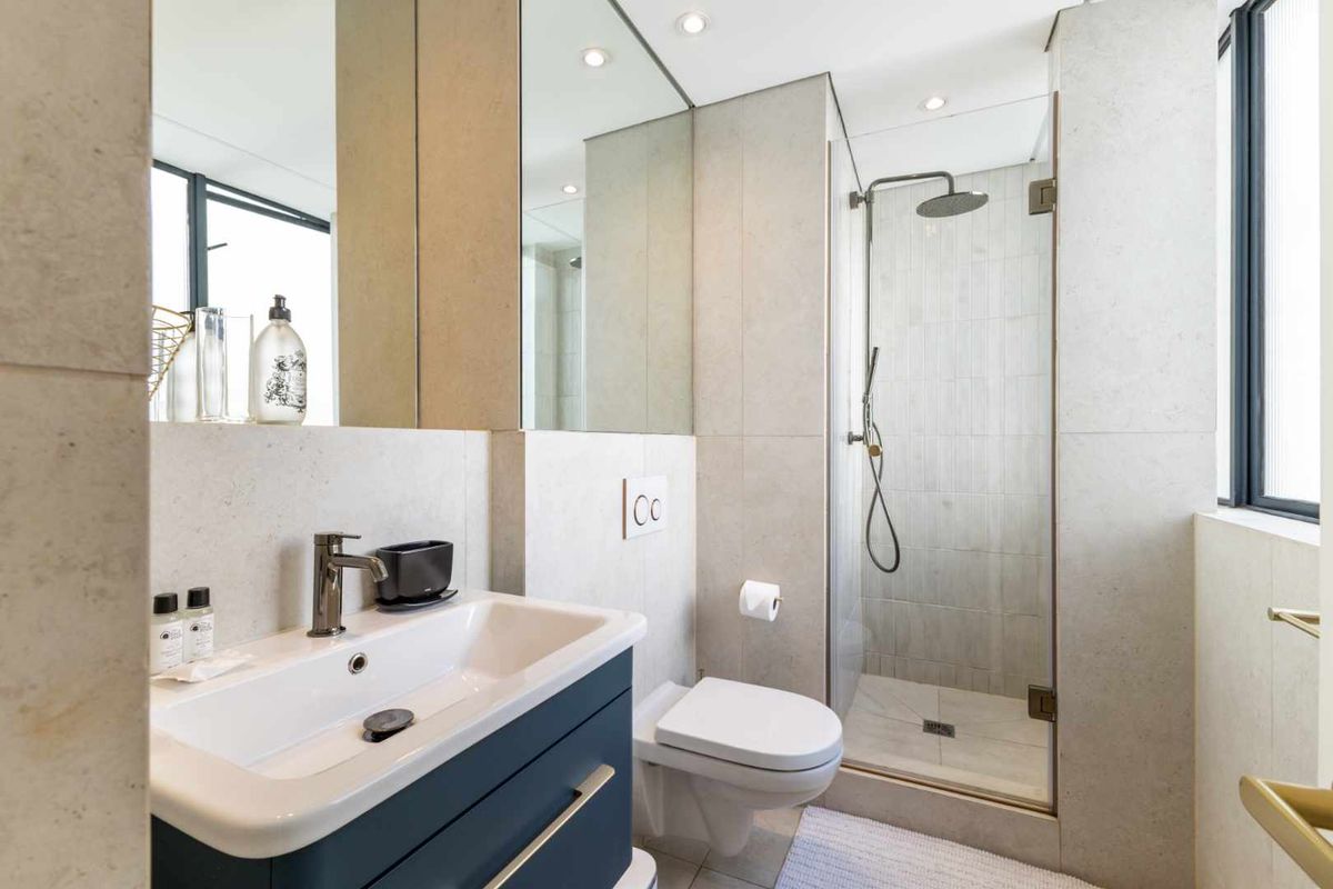 Modern bathroom featuring a sleek vanity, wall-mounted toilet, and a glass-enclosed shower with contemporary fixtures and neutral stone-look tiling.