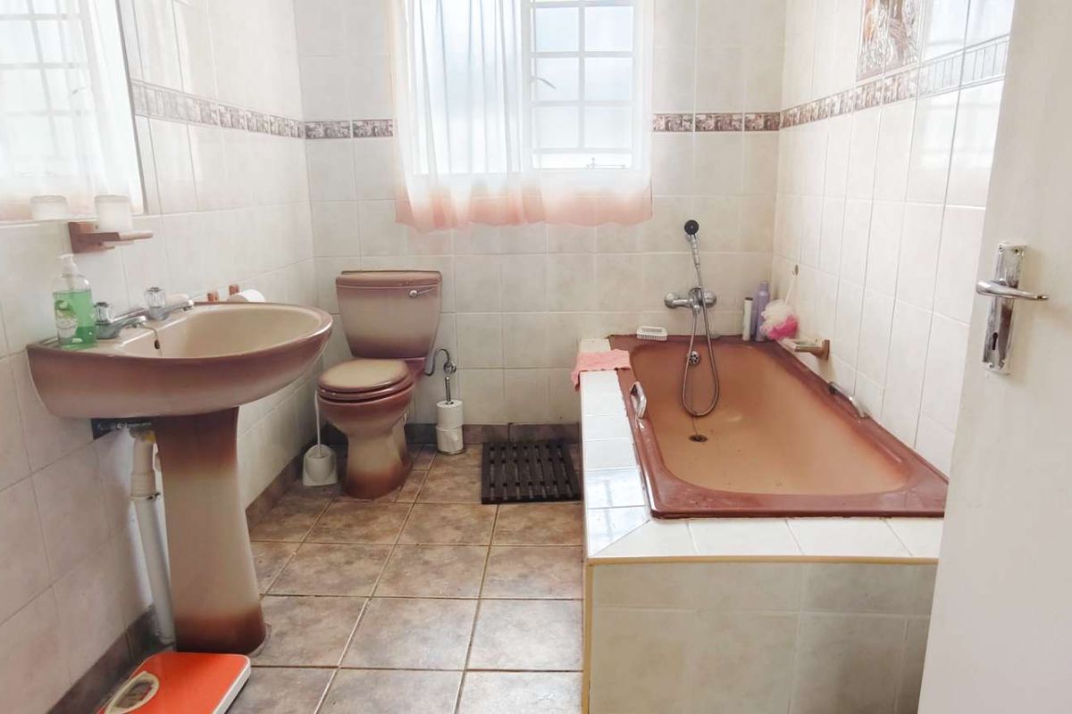 A dated bathroom featuring a brown pedestal sink, matching toilet, and a tiled bathtub with a handheld shower attachment.