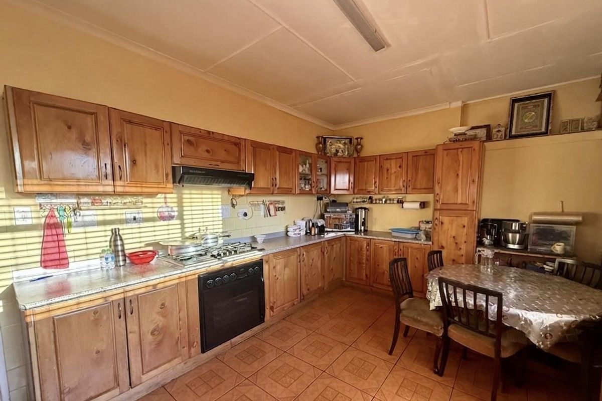 A spacious kitchen featuring traditional timber cabinetry, integrated oven and hob, tiled flooring, and a dedicated dining area.