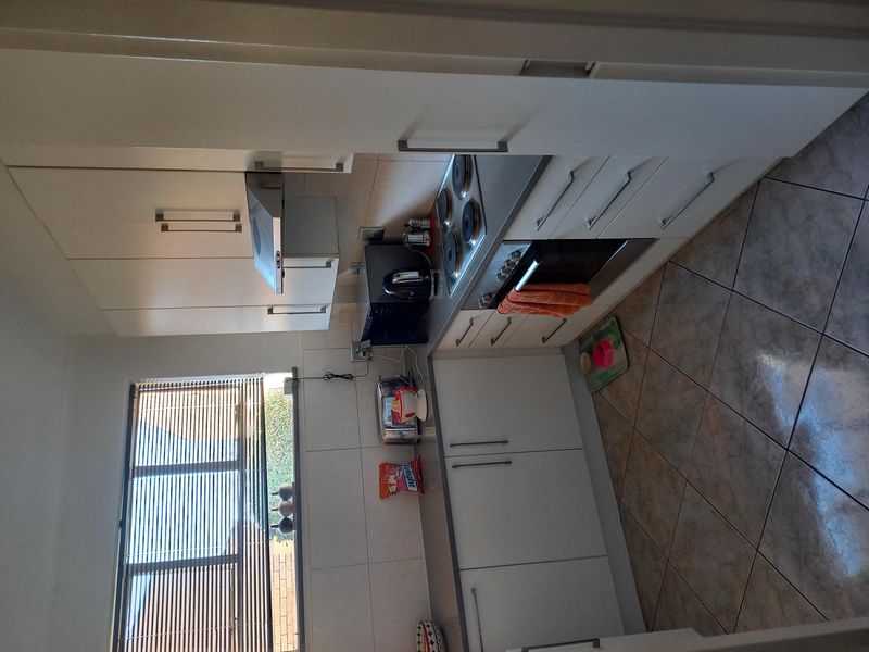 A functional kitchen featuring white built-in cabinetry, a tiled backsplash, electric hob, and oven, complemented by tiled flooring and natural light.