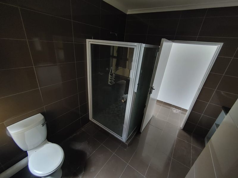 A functional bathroom featuring dark wall and floor tiles, a white toilet, and a glass-enclosed shower unit.