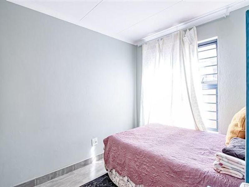 A bedroom featuring light-toned walls, tiled flooring, and a window fitted with security bars.