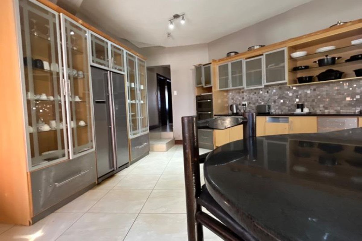 Spacious kitchen featuring extensive built-in cabinetry, glass-front display units, tiled flooring, and a central island with a dark stone countertop.