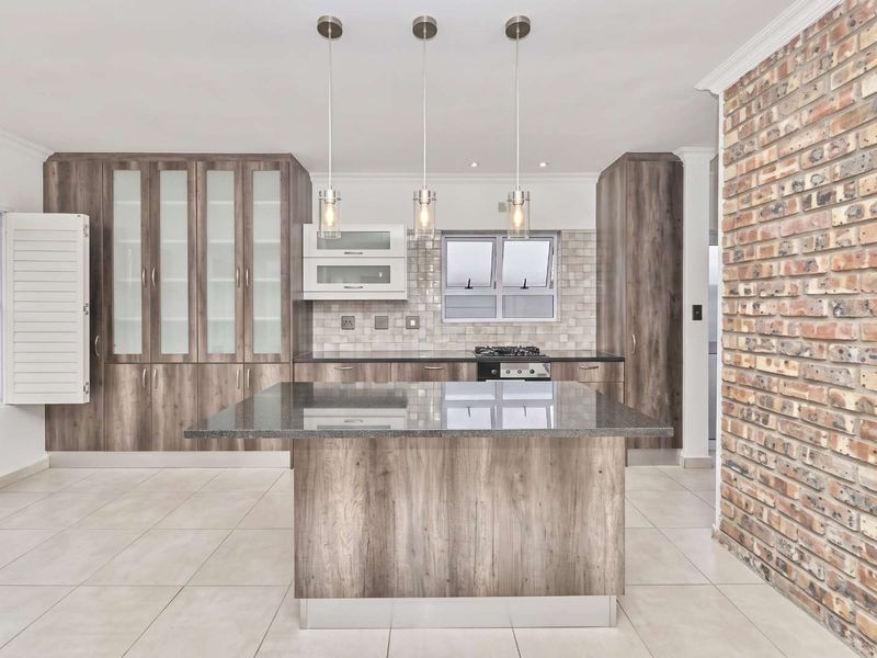 Modern kitchen featuring a central island, granite countertops, built-in cabinetry, gas hob, and a striking exposed brick feature wall.