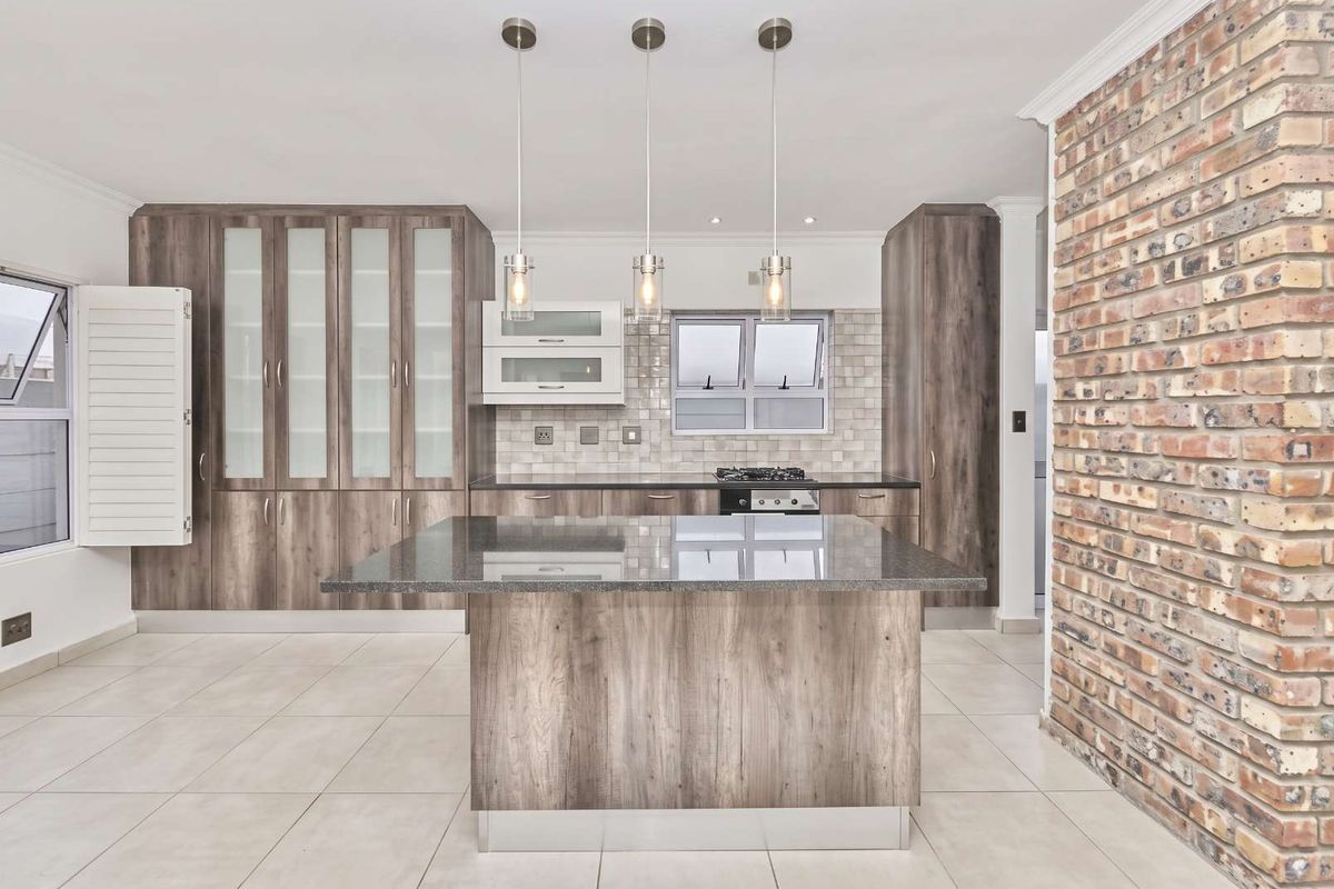 Modern kitchen featuring a central island, granite countertops, built-in cabinetry, gas hob, and a striking exposed brick feature wall.