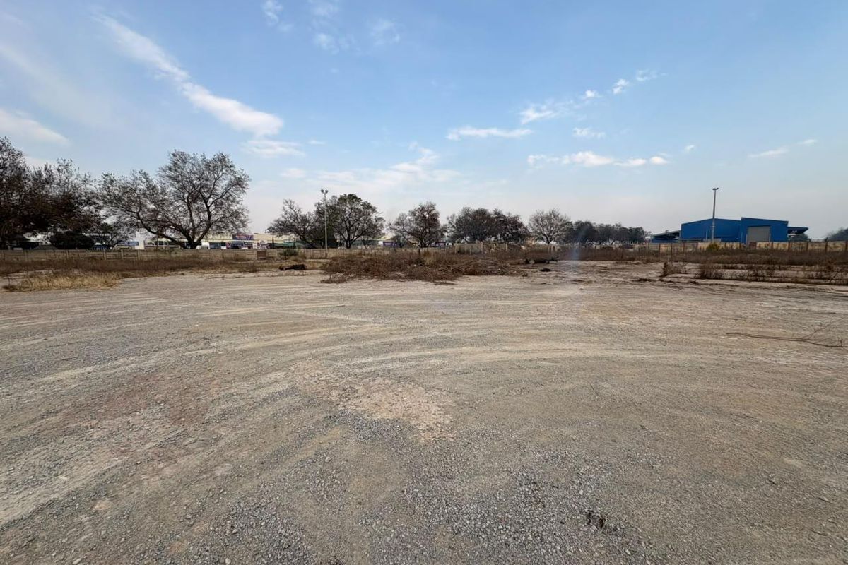 A wide-angle view of a vacant commercial land plot featuring a gravel surface and perimeter fencing, ready for development.