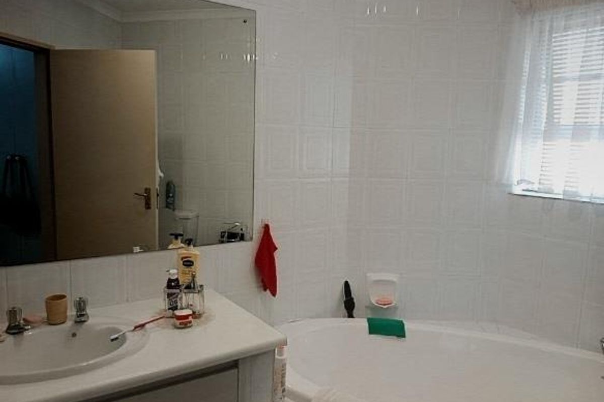 A functional bathroom featuring a built-in vanity with integrated basin, a large wall-mounted mirror, and a tiled bathtub area.