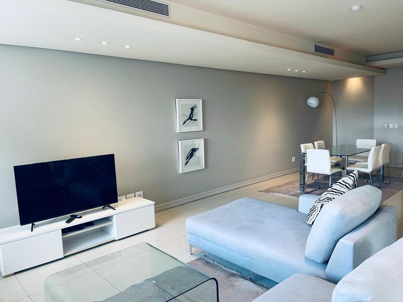 A modern open-plan living and dining area featuring neutral walls, tiled flooring, recessed ceiling lighting, and integrated ducted air conditioning.