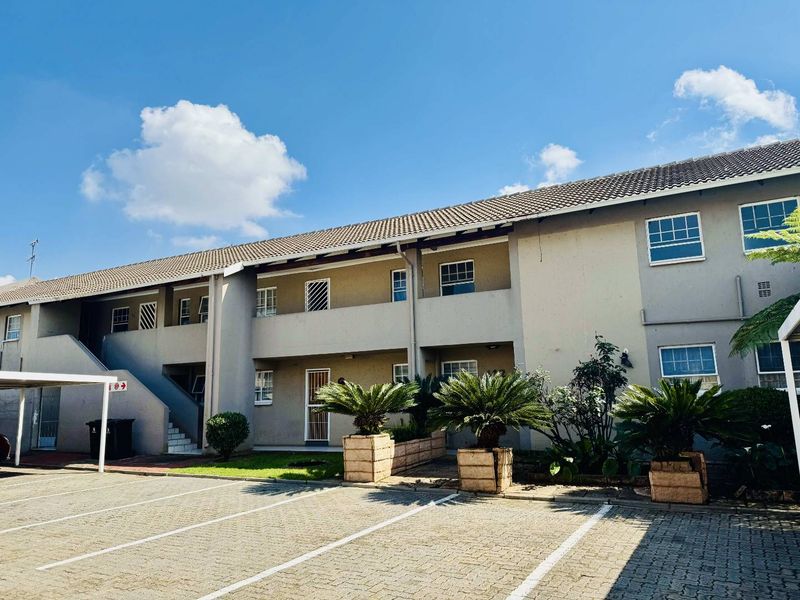 Exterior view of a multi-story apartment complex featuring a paved parking area, carports, and secure access points with security gates and bars.