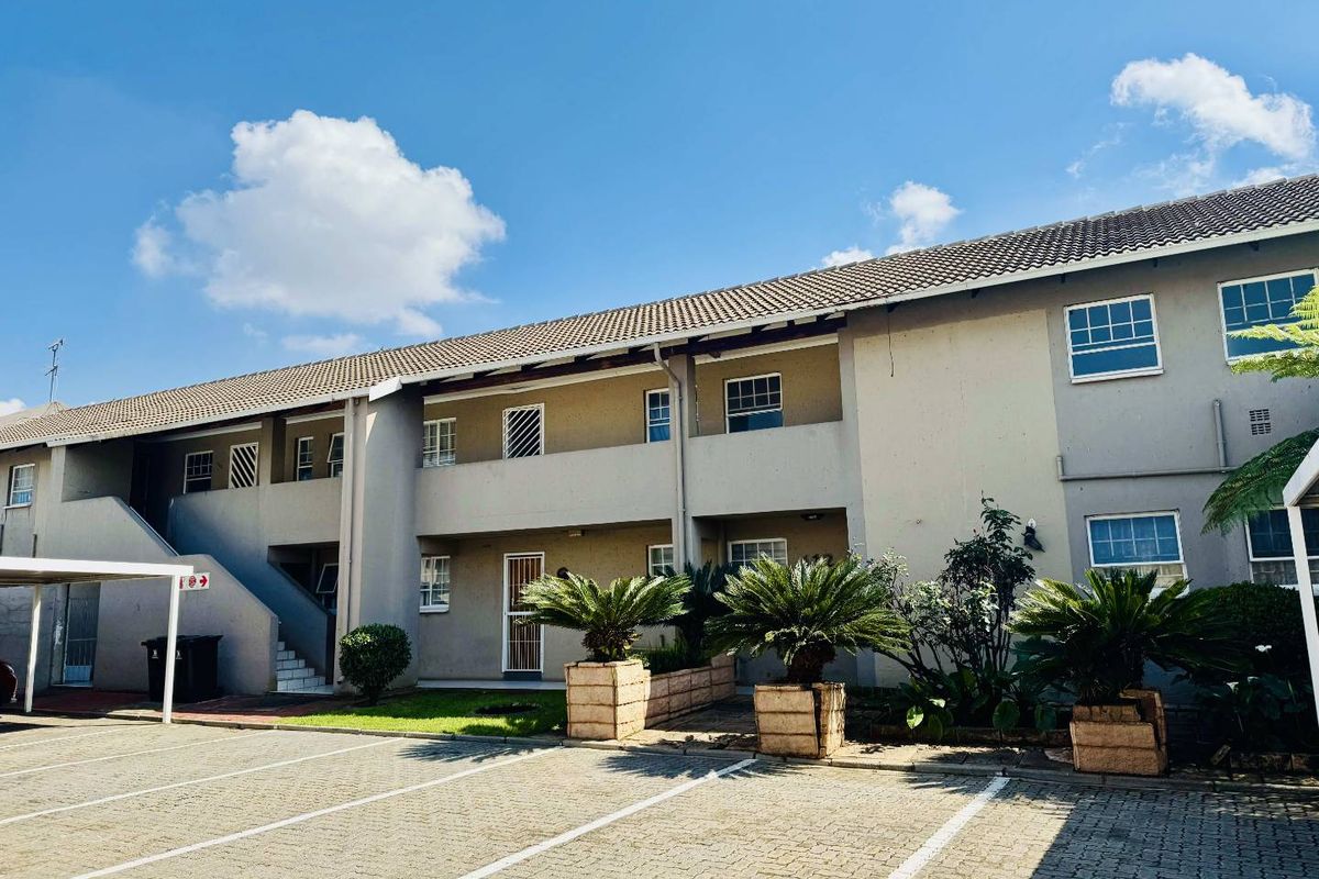 Exterior view of a multi-story apartment complex featuring a paved parking area, carports, and secure access points with security gates and bars.