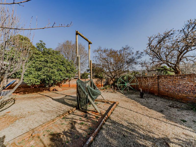 A spacious backyard garden featuring a brick boundary wall and a timber frame structure, offering potential for landscaping and outdoor improvement.