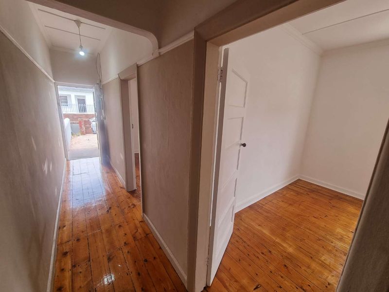 A bright hallway featuring polished hardwood flooring and traditional panelled doors, leading towards an exterior entrance.
