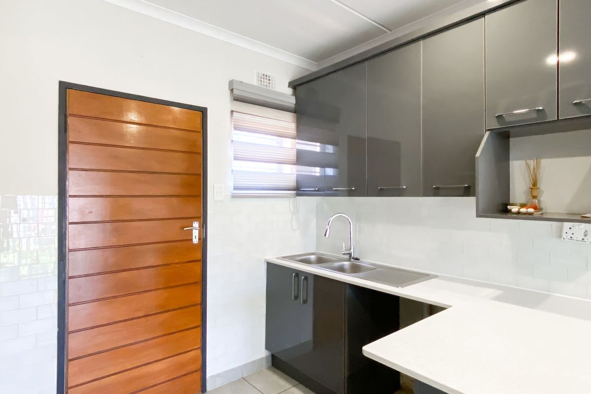 Modern kitchen featuring sleek grey cabinetry, stone countertops, a double bowl sink with mixer tap, and a clean subway tile backsplash.
