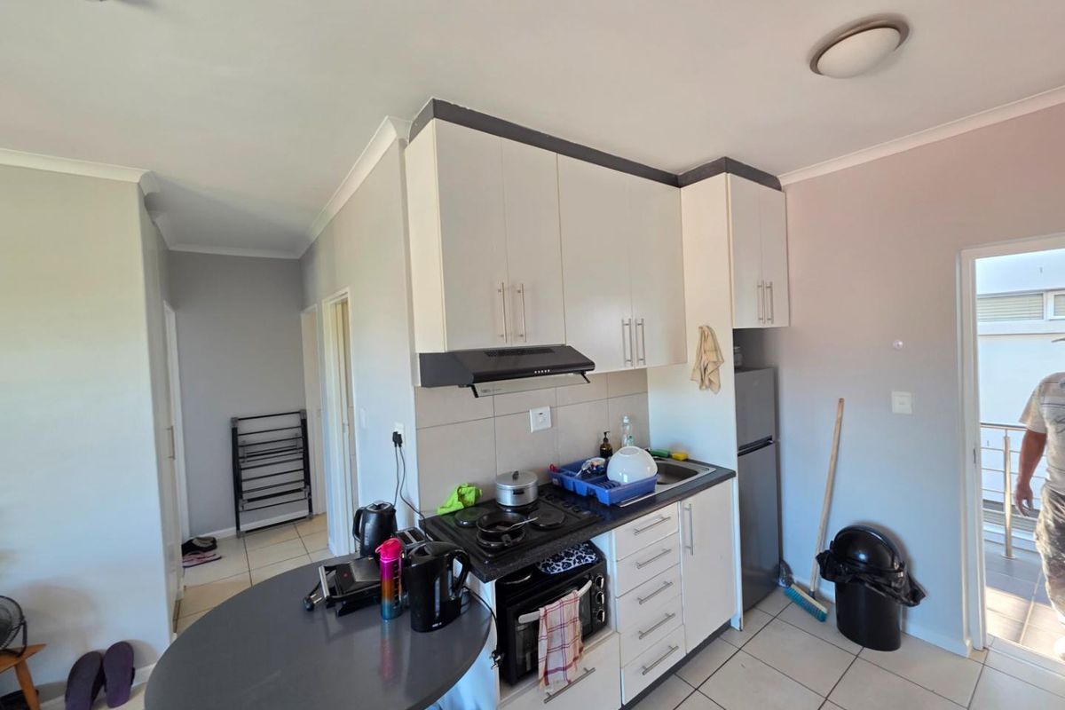 Compact kitchen featuring white cabinetry, dark countertops, a built-in hob, and an extractor fan, with an adjacent breakfast bar area.