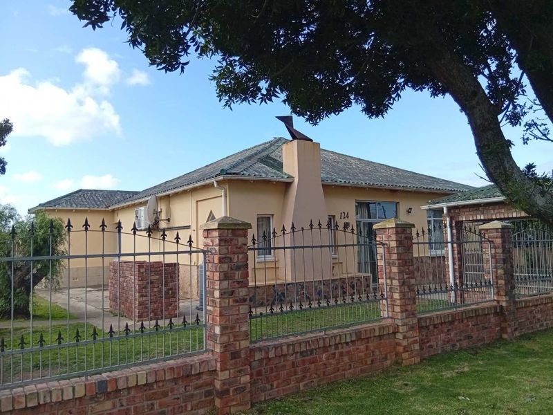Front view of a single-story house featuring a brick boundary wall, wrought iron fencing, and a tiled roof with an external chimney.