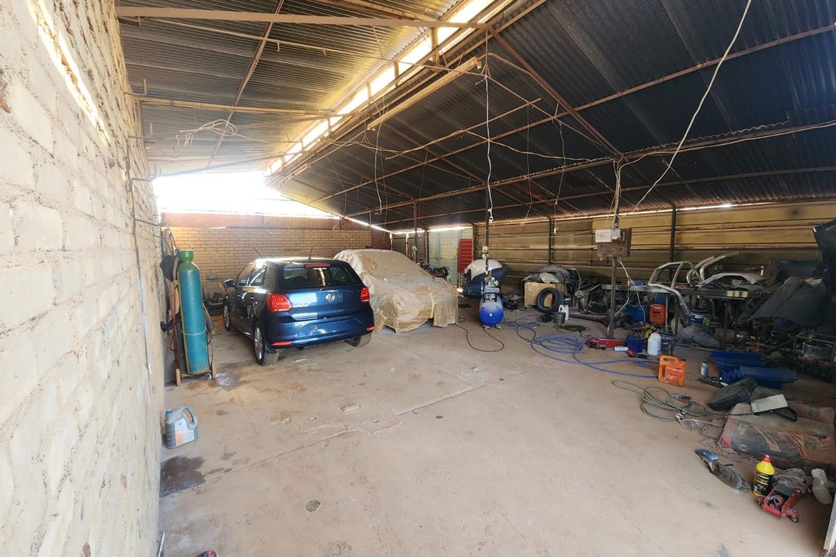 A large, industrial-style workshop or garage space featuring exposed brick walls, a corrugated metal roof, and concrete flooring.