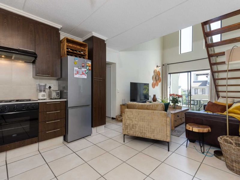 Open-plan living area featuring a modern kitchen with dark wood cabinetry, tiled floors, and a staircase leading to the upper level.