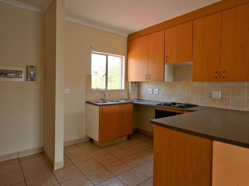 A functional kitchen featuring laminate cabinetry, tiled backsplash, built-in hob, and ceramic floor tiles in an open-plan layout.