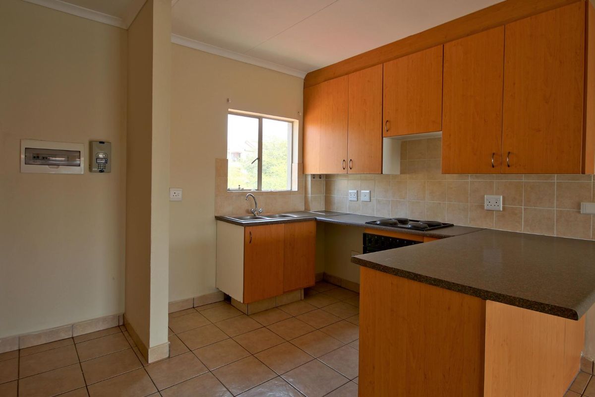 A functional kitchen featuring laminate cabinetry, tiled backsplash, built-in hob, and ceramic floor tiles in an open-plan layout.
