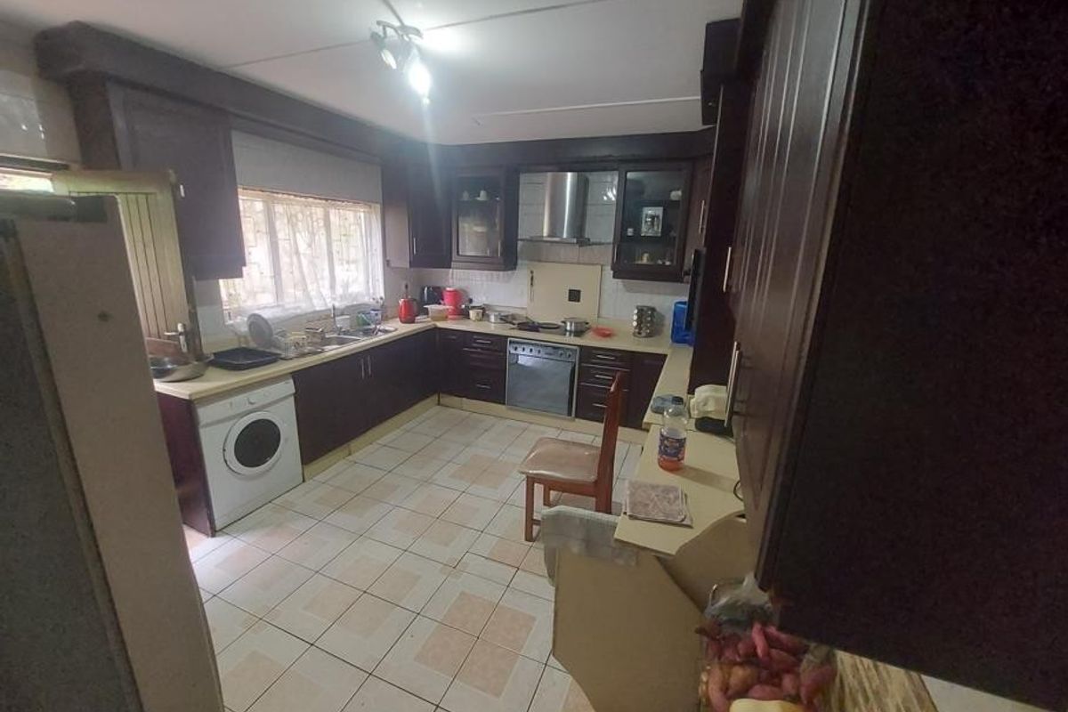 A functional kitchen featuring dark wood cabinetry, stainless steel appliances, tiled flooring, and ample counter space, offering potential for a modern cosmetic update.