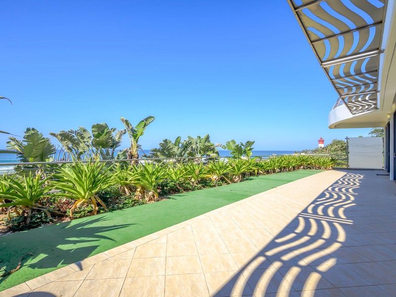 Spacious balcony featuring tiled flooring, artificial grass, a metal pergola, and a glass balustrade with scenic ocean and lighthouse views.
