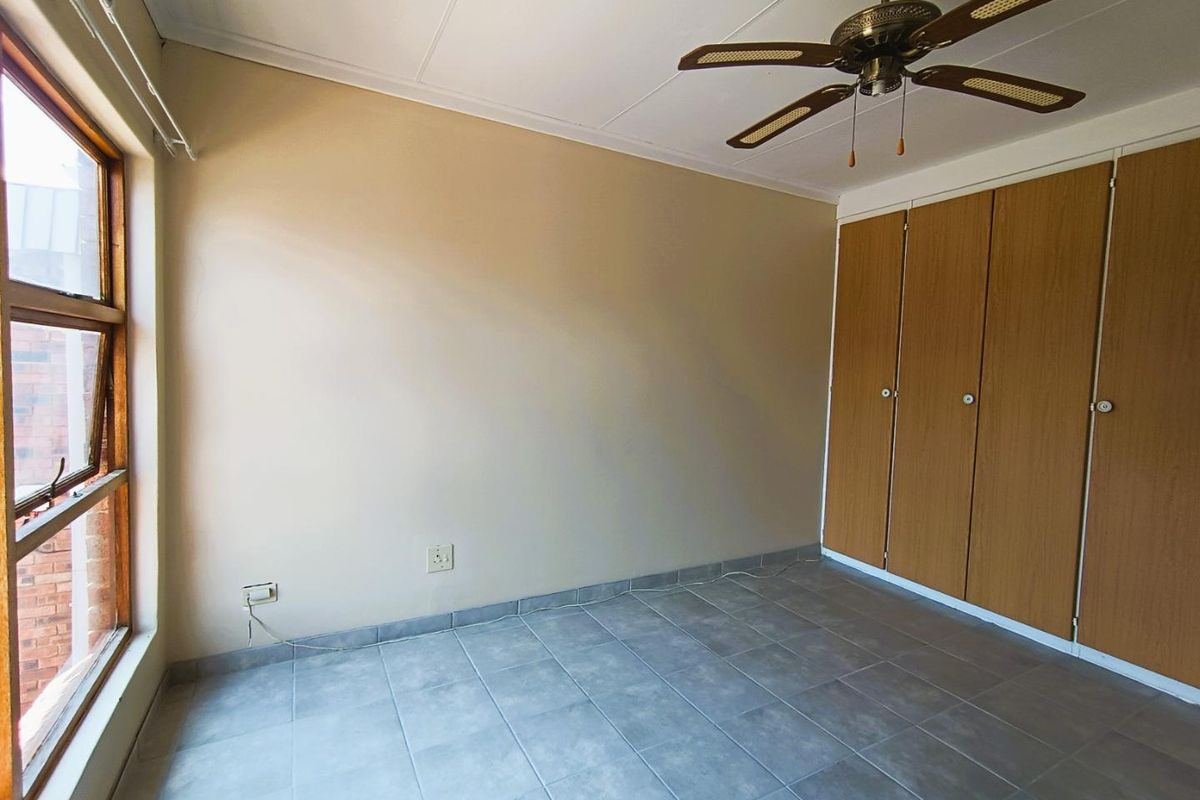 A bedroom featuring tiled flooring, built-in wooden cupboards, and a ceiling fan.