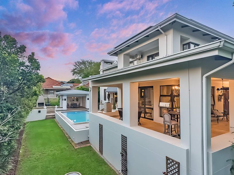 A beautifully maintained rear exterior featuring a covered patio, a swimming pool, and a separate outdoor entertainment area with a built-in braai.