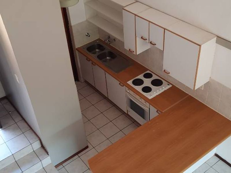 A compact, functional kitchen featuring white cabinetry, laminate countertops, an electric hob, and tiled flooring, presented in a clean, empty state.