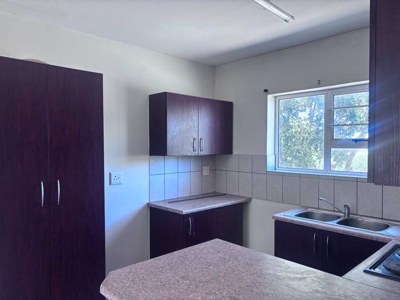 A functional kitchen featuring dark wood-finish cabinetry, laminate countertops, a double bowl sink, and a tiled backsplash with natural light from the window.