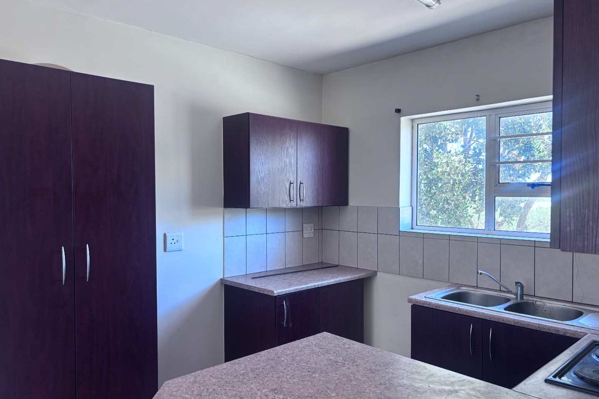 A functional kitchen featuring dark wood-finish cabinetry, laminate countertops, a double bowl sink, and a tiled backsplash with natural light from the window.