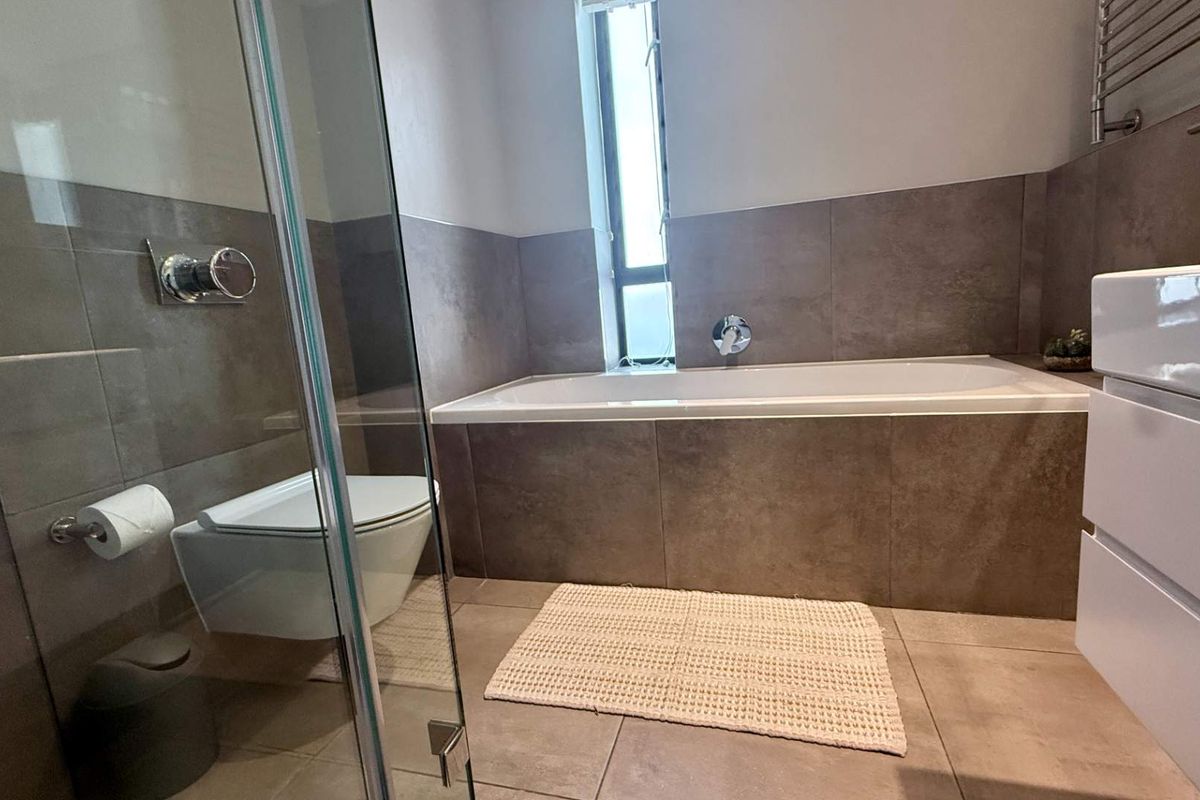 Modern bathroom featuring a built-in bathtub, glass-enclosed shower, wall-mounted toilet, and contemporary neutral tiling throughout.