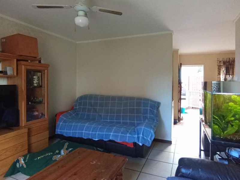 A living room area featuring tiled flooring and a ceiling fan, with an open layout leading towards an exterior entrance.