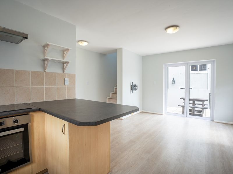 Open-plan kitchen and living area featuring light laminate flooring, built-in oven with extractor, and glass sliding doors leading to an outdoor patio space.