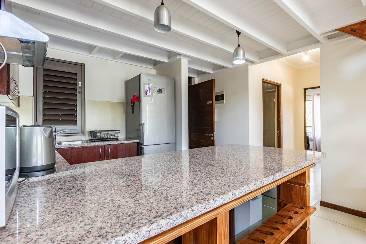 A functional kitchen featuring granite countertops, wooden cabinetry, and an exposed beam ceiling with pendant lighting, offering a practical and well-lit workspace.